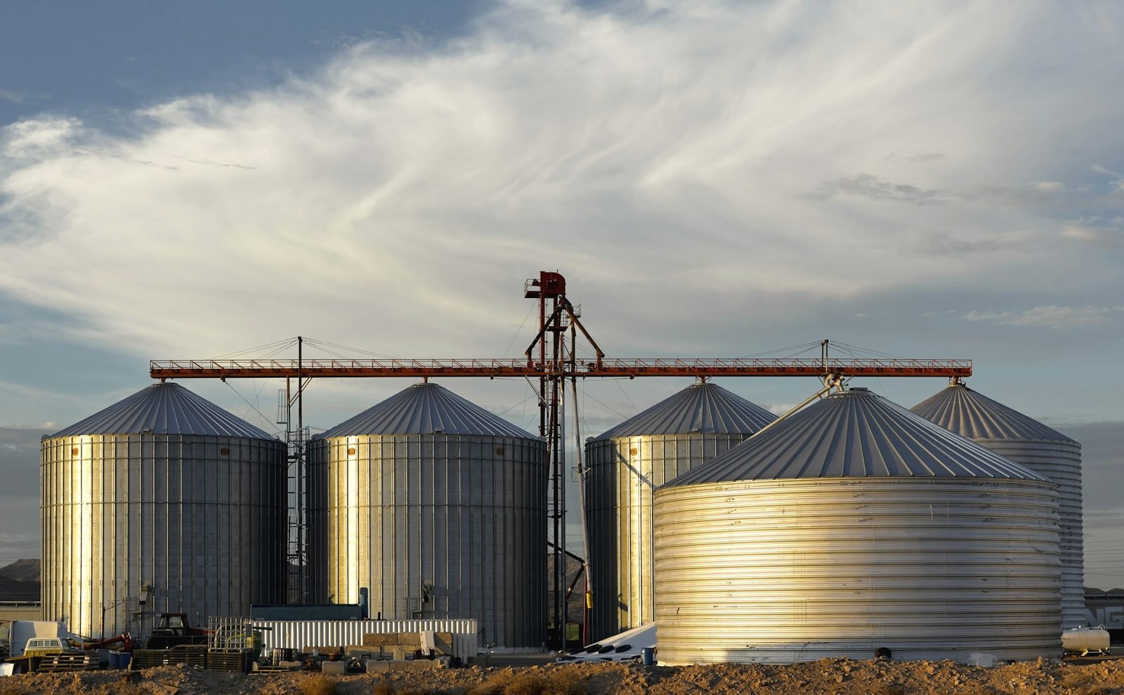 Steel grain bins and an overhead conveyor in late sun